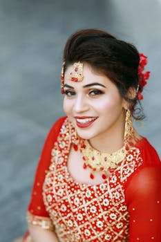 A beautiful woman in a red saree and gold jewelry smiling warmly for a portrait.